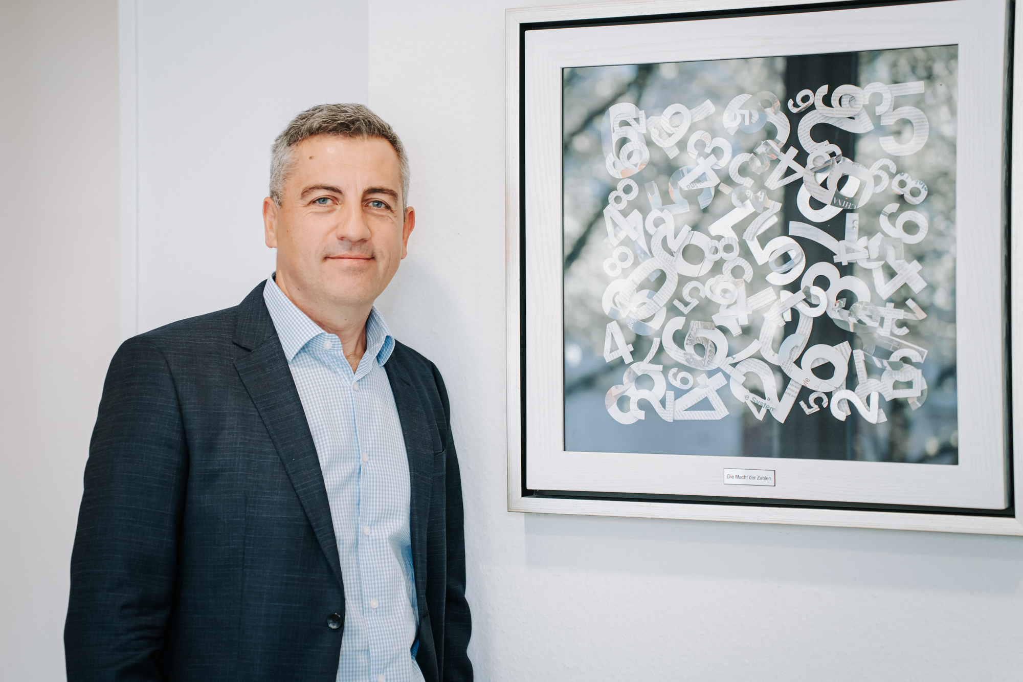 Steuerberater im Anzug vor einem abstrakten Kunstwerk im Büro